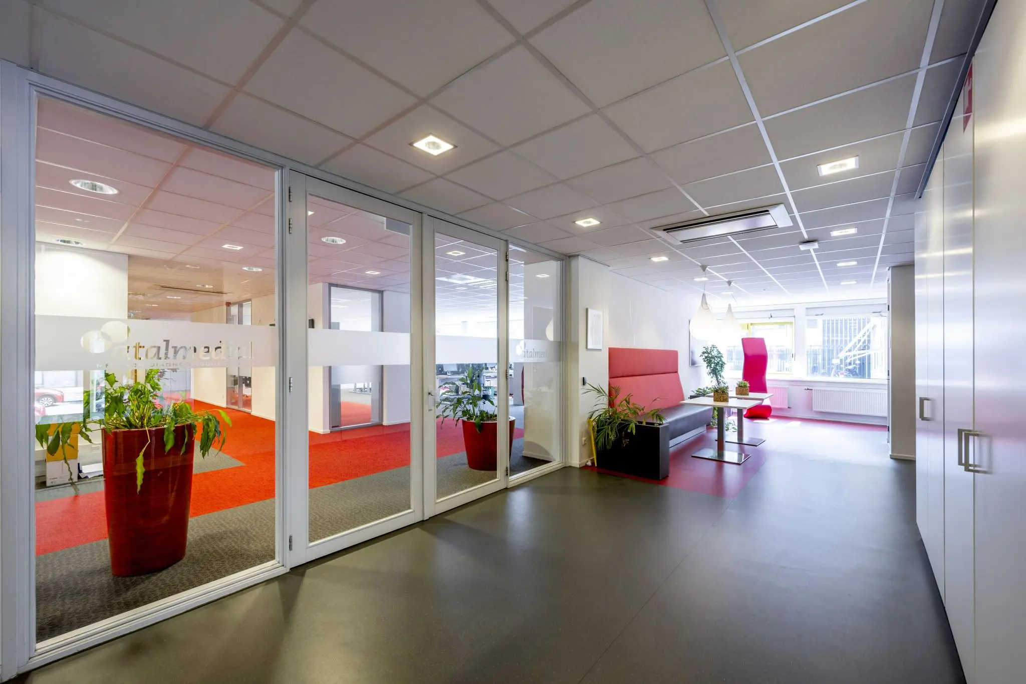 Moderne wachtruimte en kantoorentree aan de Jan Tooropstraat met glazen wanden, rode accenten en kantoormeubilair.